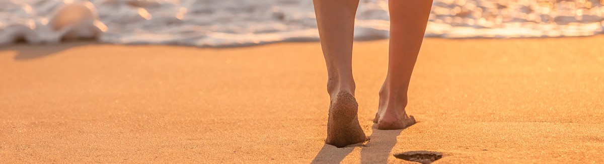 A persons feet walking on the beach towards the sea